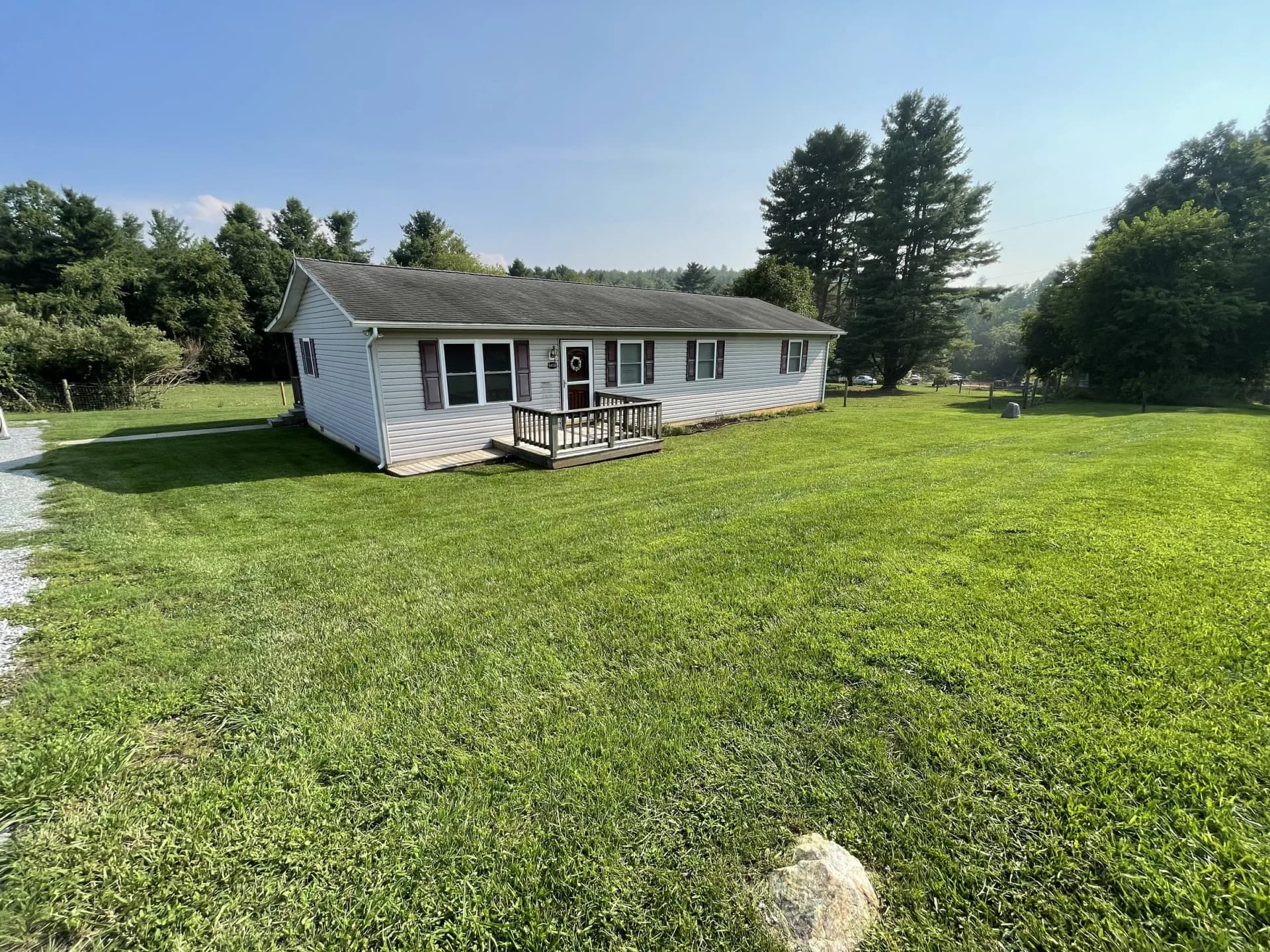 Neatly mowed green lawn surrounding a light-colored single-story home with a small front deck.
