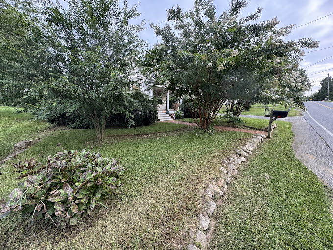 Residential front yard landscaping with mature trees and decorative stone edging